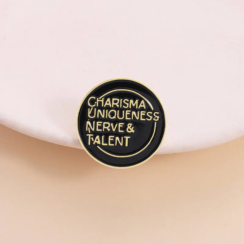 A round black lapel pin with gold lettering that reads Charisma Uniqueness Nerve & Talent