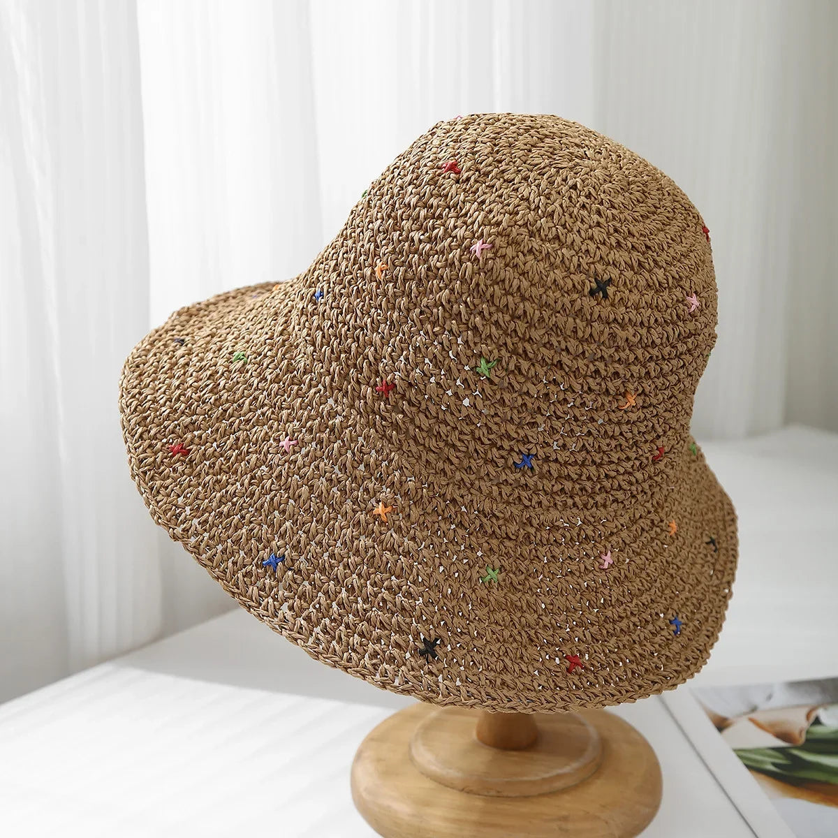 Vista cercana de un sombrero de paja panameña tejido a crochet con adornos coloridos sobre un soporte de madera.
