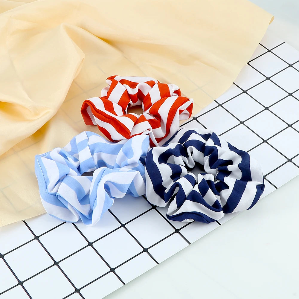 Three colorful knitted hair scrunchies in red and white, blue and white, and navy and white, displayed on a yellow fabric.