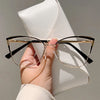 Un par de gafas de computadora con montura dorada estilo ojo de gato sobre una funda de cuero blanco.