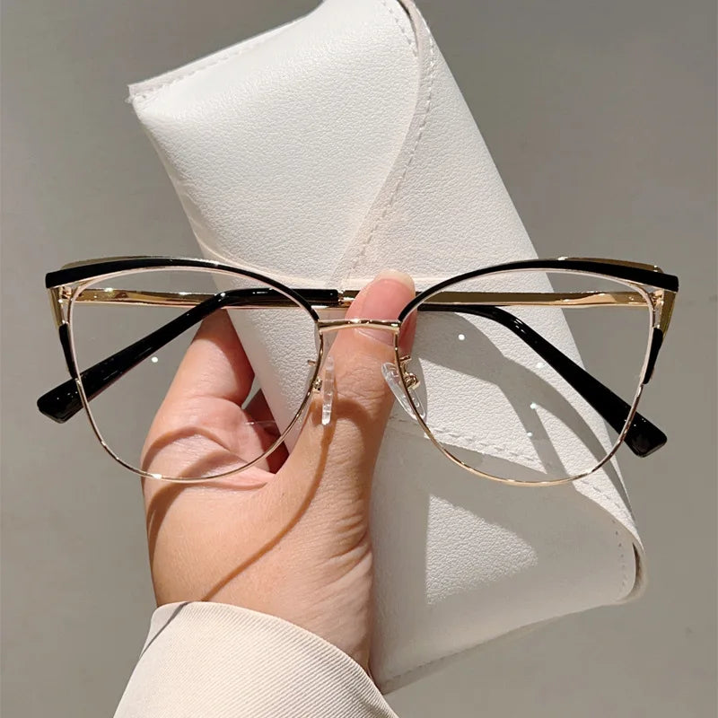 Un par de gafas de computadora con montura dorada estilo ojo de gato sobre una funda de cuero blanco.