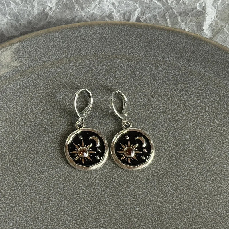 Silver hoop earrings featuring a black disc design with a gold sun and crescent moon motif.