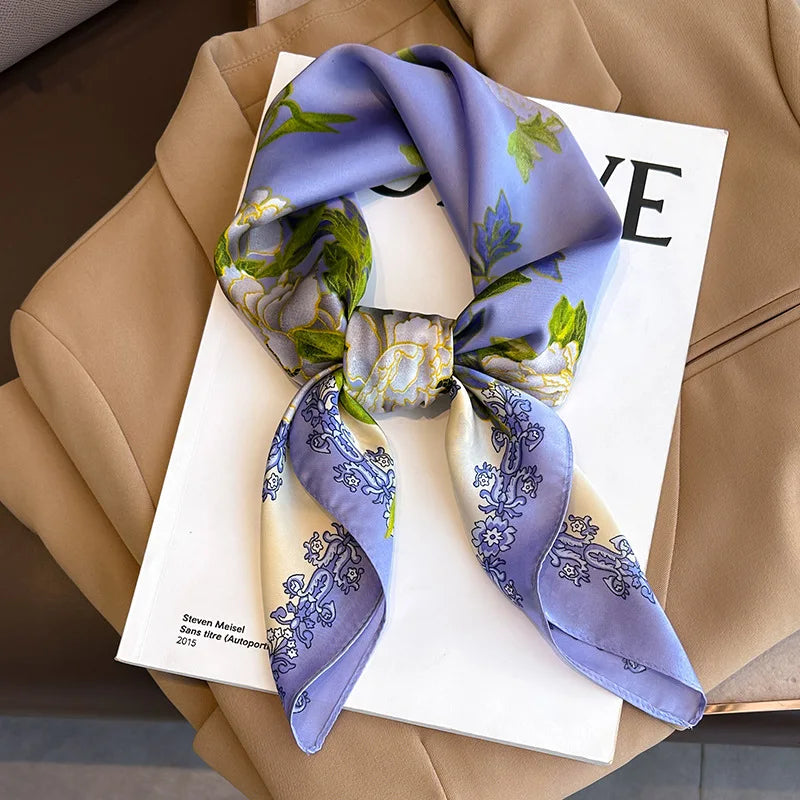 A purple silk scarf tied in a bow, featuring floral patterns, displayed on a white card against a beige blazer.