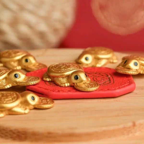 A collection of gold turtle charms resting on a red felt pad on a wooden surface.