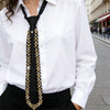 A close-up of an elegant black necktie adorned with gold and clear rhinestones worn by a woman in a white shirt.