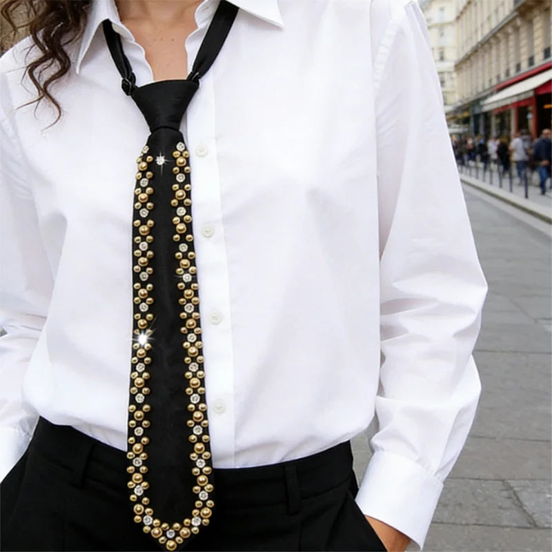 A close-up of an elegant black necktie adorned with gold and clear rhinestones worn by a woman in a white shirt.