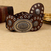 A stack of dark brown leather oval waist belts with silver accents resting on a beige fabric.