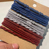 Eine Sammlung von Boho-Elastband-Haarbändeln in verschiedenen Blautönen, Grautönen und Weinrot auf einem Kraftpapier-Etikett.