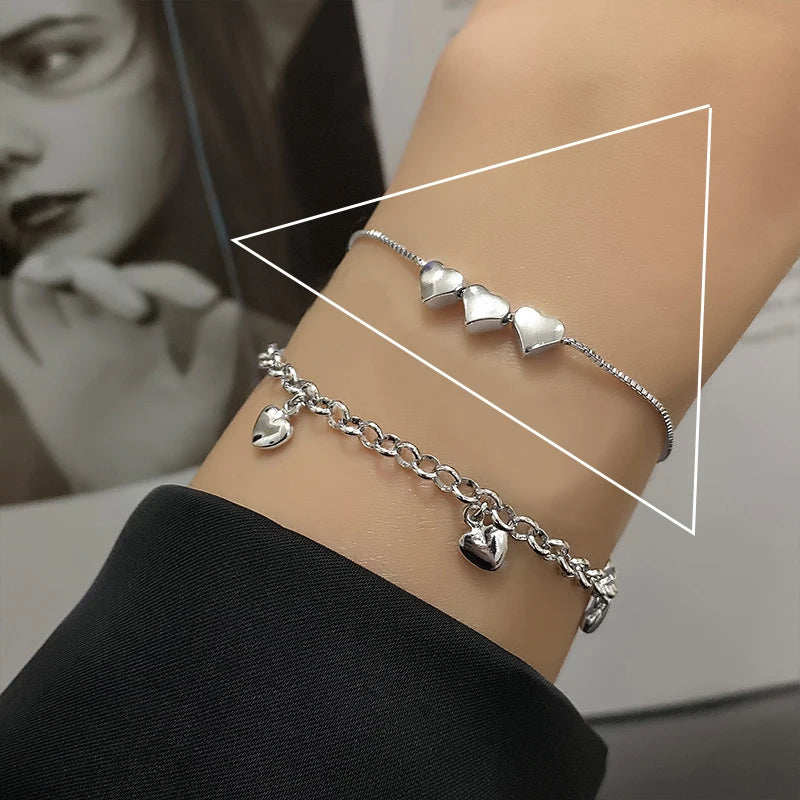 A close-up of a sterling silver double heart charm bracelet worn on a wrist.