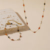 A delicate gold chain necklace featuring various colored beads including orange, black, and light blue stones.
