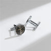 A close-up shot of elegant silver cufflinks with a round watch face design on a white background.