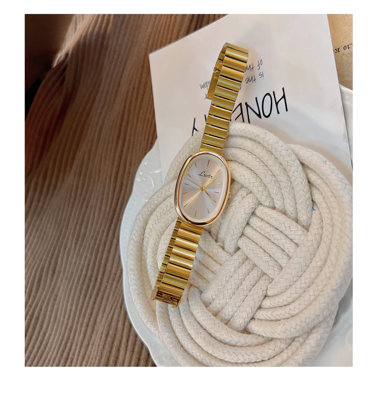 Montre et bracelet en quartz doré exposés sur fond blanc à côté d'une épaisse corde de fil crème.