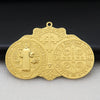 A gold-colored Saint Benedict protection medal with a cross and religious symbols, displayed on a dark background.