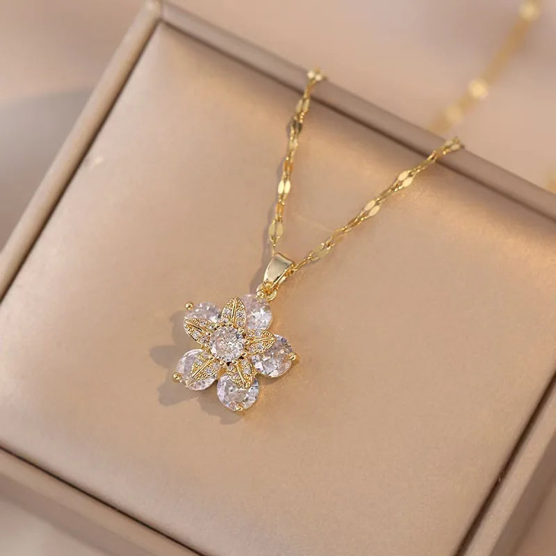 Un délicat collier en or avec un pendentif de fleur de zircon scintillante, présenté dans une boîte de couleur claire.