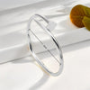 Silver stainless steel bangle bracelet with a four-leaf clover charm shown on a white surface.