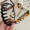 A hand holds a set of fashion acetate toothed headbands in black and amber tones.