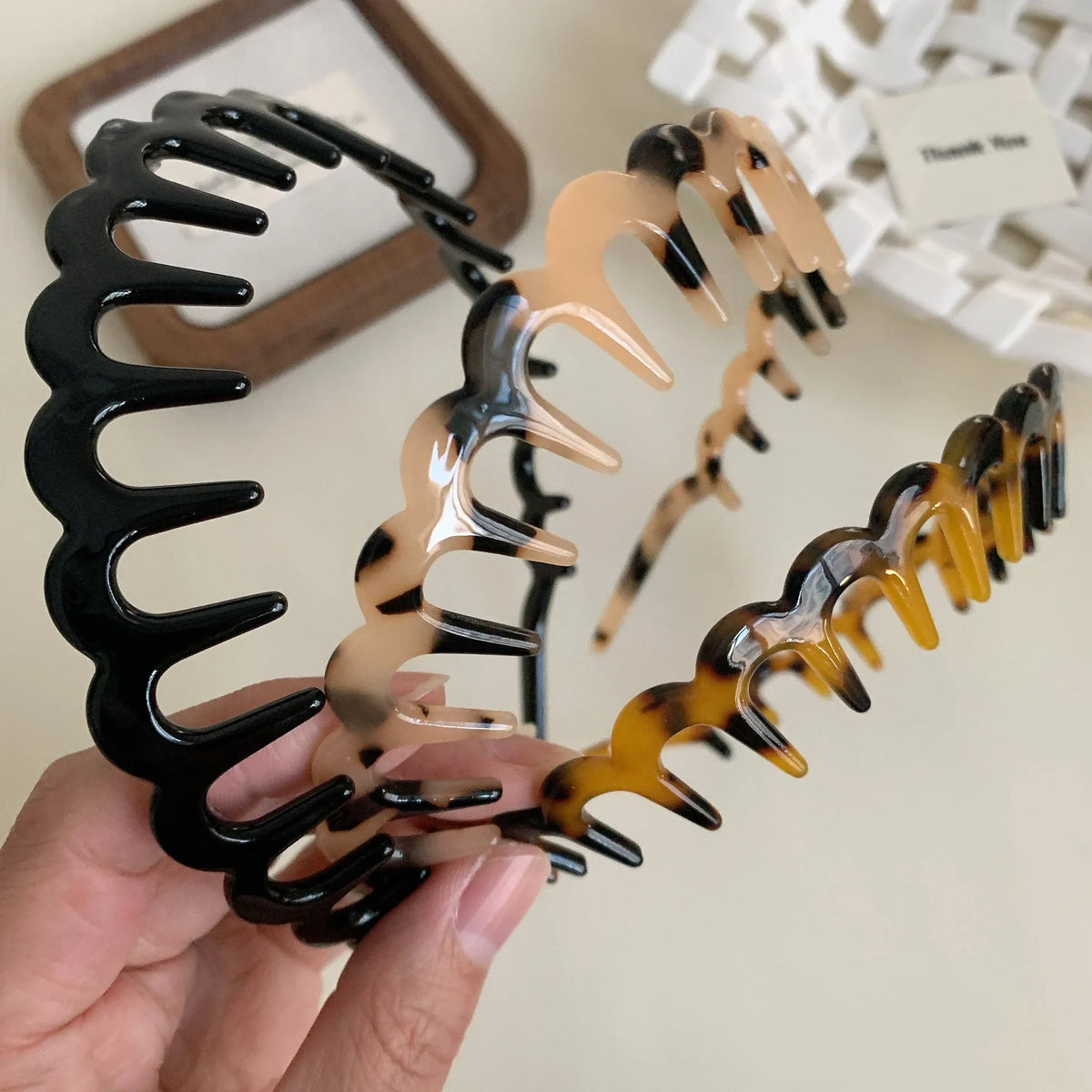 A hand holds a set of fashion acetate toothed headbands in black and amber tones.