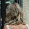 A woman with light blonde hair shows the back of her head adorned with a delicate crystal chain bridal hair accessory.
