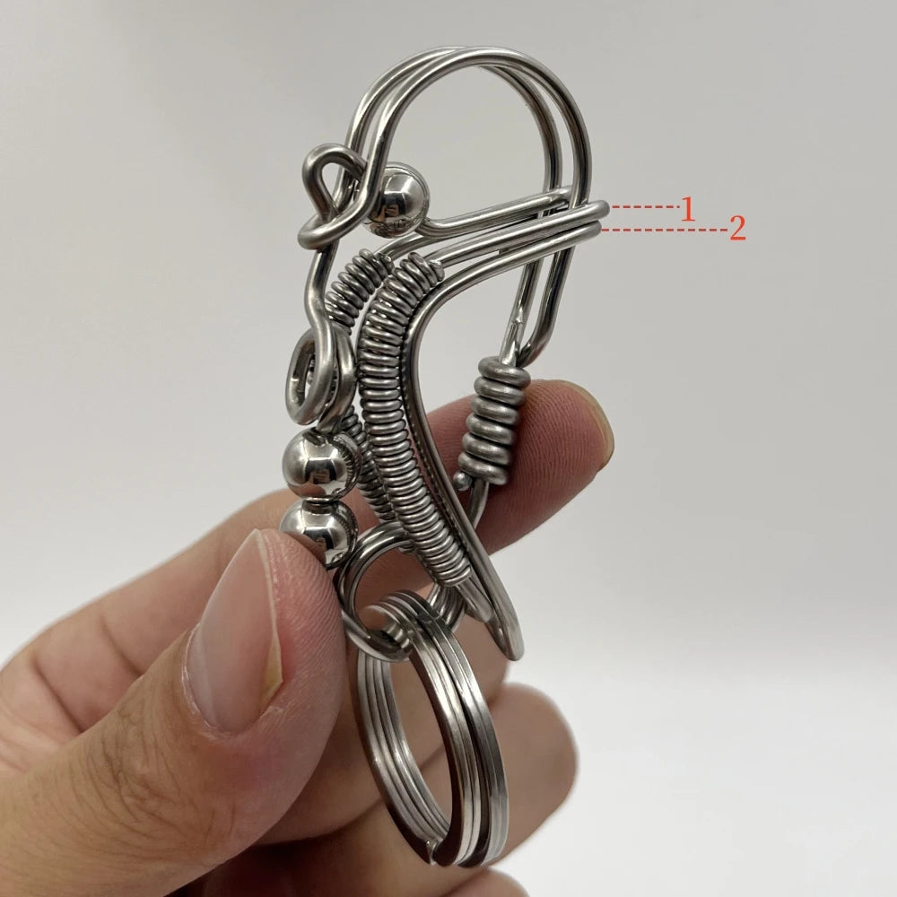 Une main tient un porte-clés mécanique en acier inoxydable avec un mécanisme à ressort et une boucle.