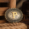 A vintage western belt buckle with a gold-toned design and intricate engraving resting on a brown textile.