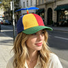 A woman wearing a funny multicolor propeller hat with blue, yellow, red, and green panels on a city street.