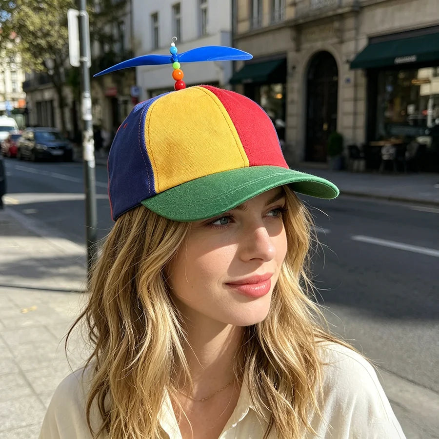 A woman wearing a funny multicolor propeller hat with blue, yellow, red, and green panels on a city street.