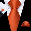 A close-up view of an orange silk jacquard tie and white dress shirt collar against a black background.
