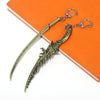 A gold-colored dagger keyring pendant with a decorative handle and a silver clasp, resting on an orange notebook.
