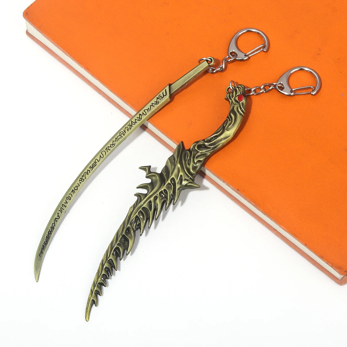 A gold-colored dagger keyring pendant with a decorative handle and a silver clasp, resting on an orange notebook.