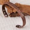 Gros plan d'un ensemble de bracelets floraux en cuivre plaqué antique posé sur un tissu clair à côté d'un morceau de bois.