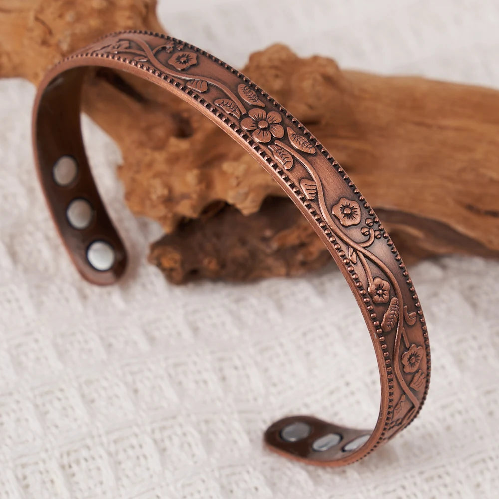 Gros plan d'un ensemble de bracelets floraux en cuivre plaqué antique posé sur un tissu clair à côté d'un morceau de bois.
