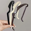 Three sleek hair sticks in black, cream, and brown are held by a hand.
