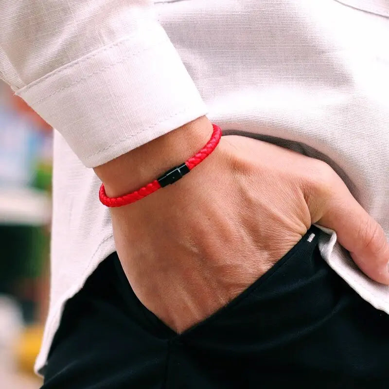 A close-up of a hand wearing a red thread charm bracelet on the wrist, visible under a white sleeve.