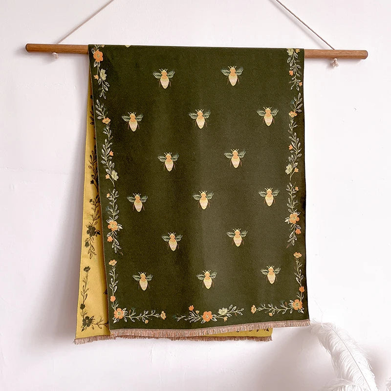 A dark olive green pashmina shawl featuring a floral print of small golden bees.