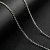 Collier de chaîne cubaine en acier inoxydable argenté, gros plan, posé sur une surface sombre.