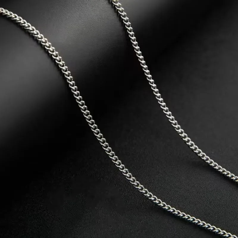 Collier de chaîne cubaine en acier inoxydable argenté, gros plan, posé sur une surface sombre.