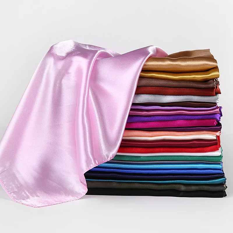 Una pila de pañuelos de seda satinada de varios colores, incluyendo un pañuelo rosa grande, mostrados contra un fondo blanco.