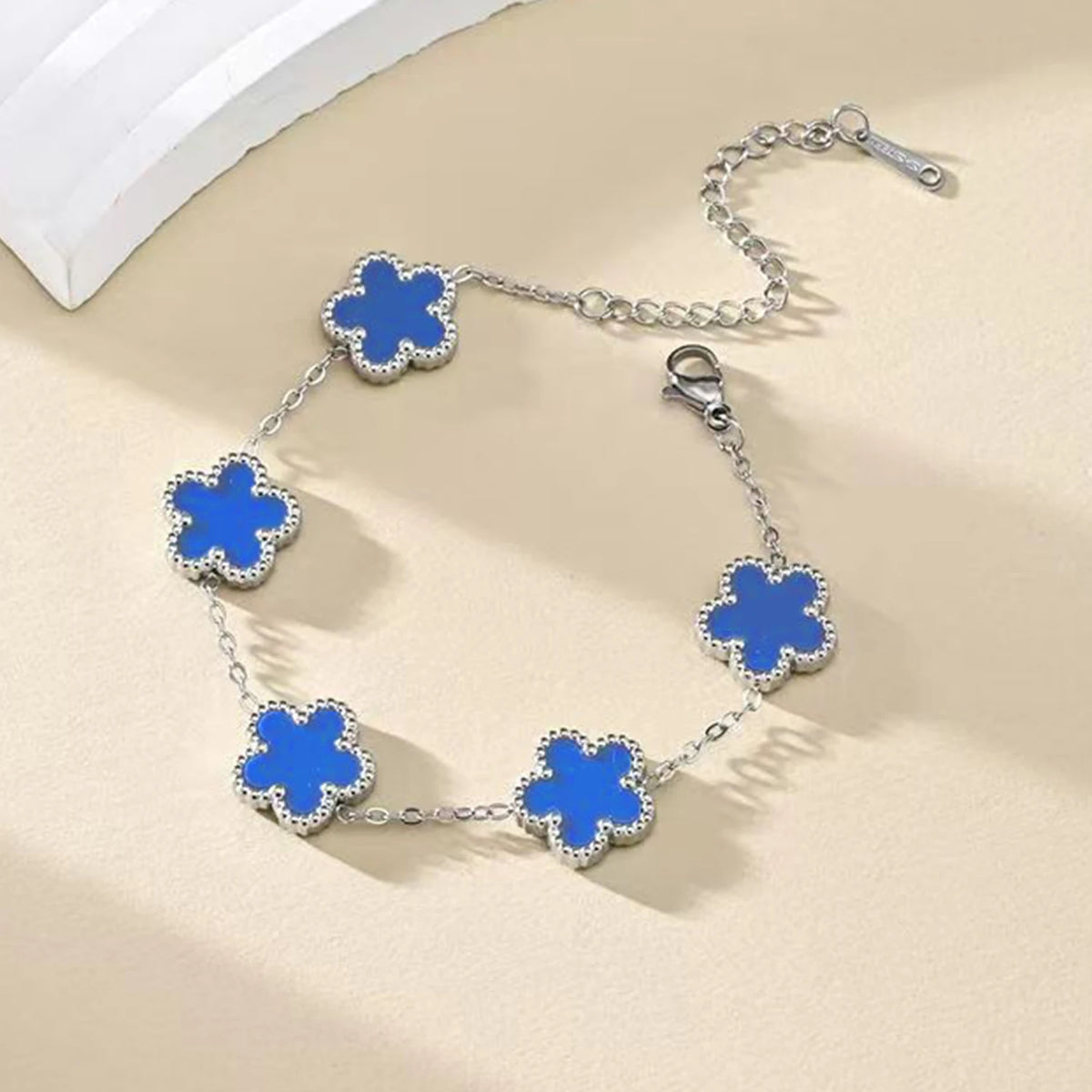 A silver gold plated stainless steel bracelet featuring four blue floral charms on a chain.