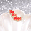 Insignia de esmalte dorado con letras rojas que dicen 'No Me Diga' en un objeto de cerámica blanca.