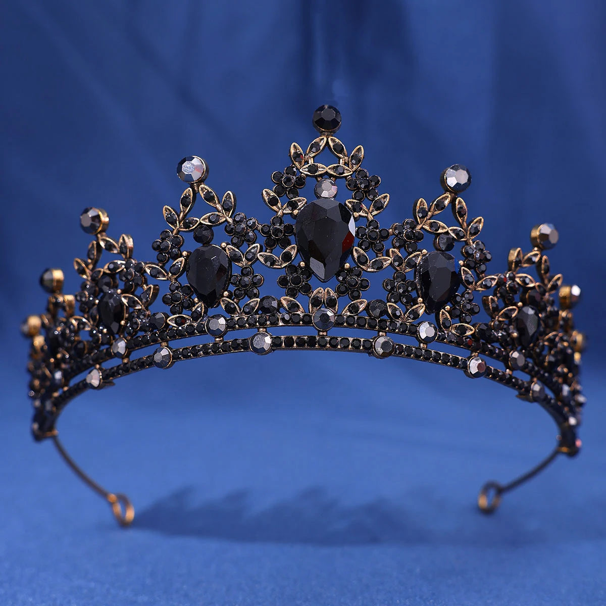 A dark metal crown set featuring black stones and clear crystals, displayed against a blue background.