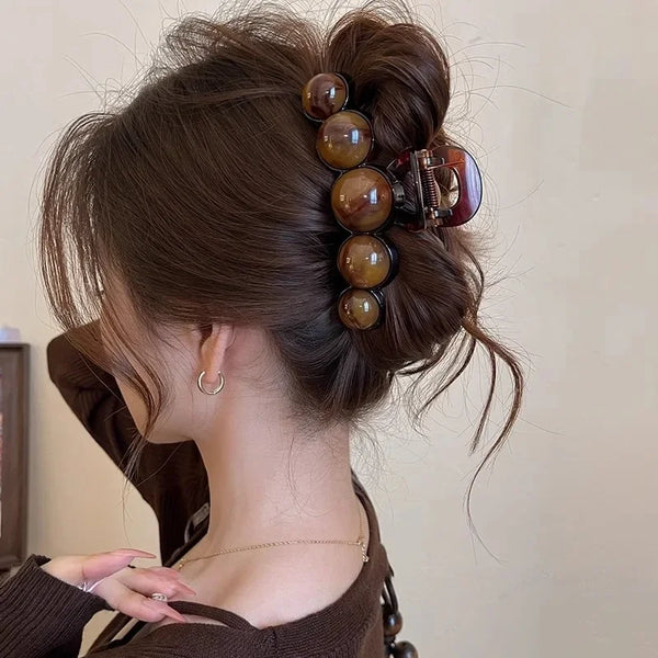 A woman's dark brown hair is styled in an updo with a retro gradient beaded hair claw clip featuring amber and tortoiseshell 