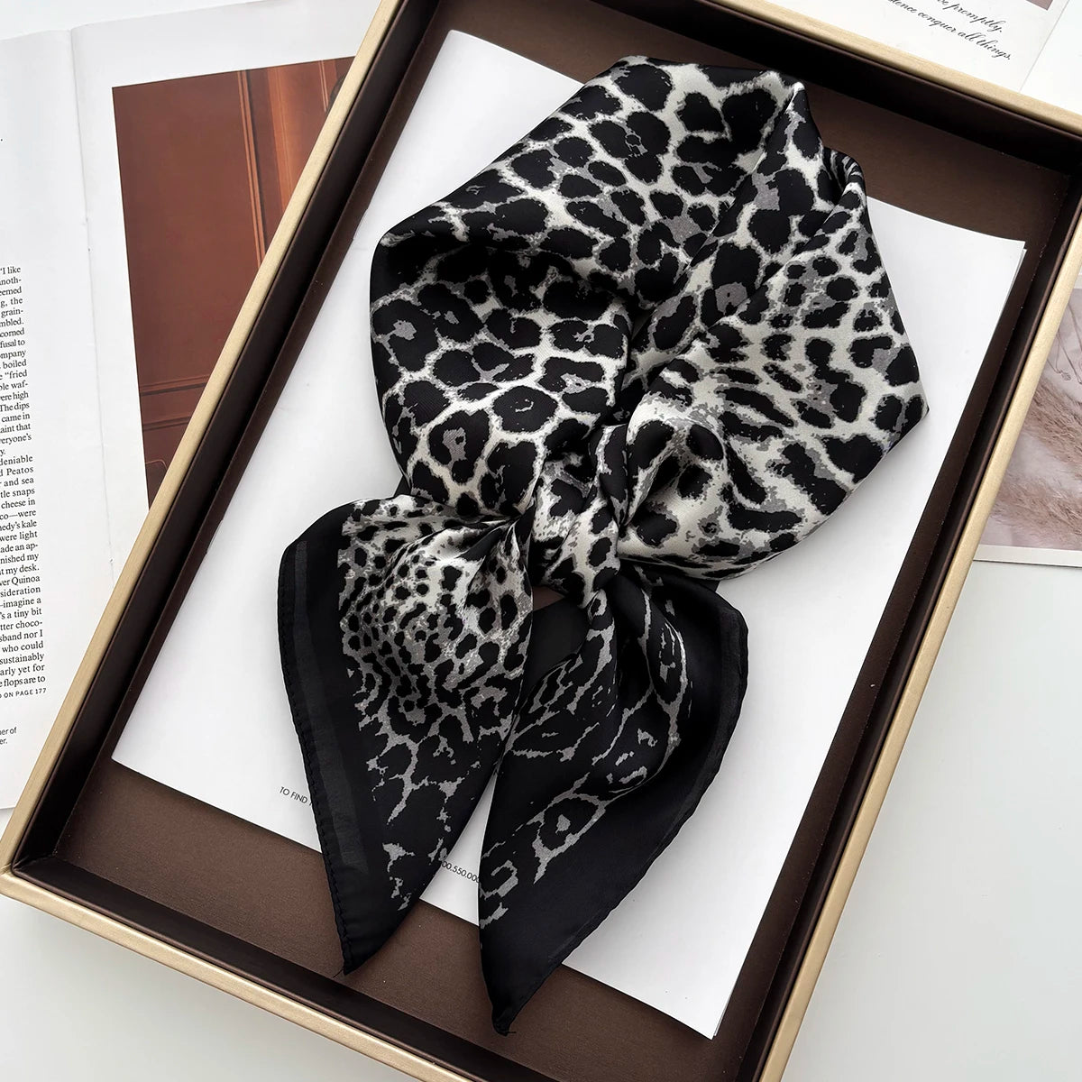 A black and white leopard print silk scarf tied in a bow displayed in a wooden frame.