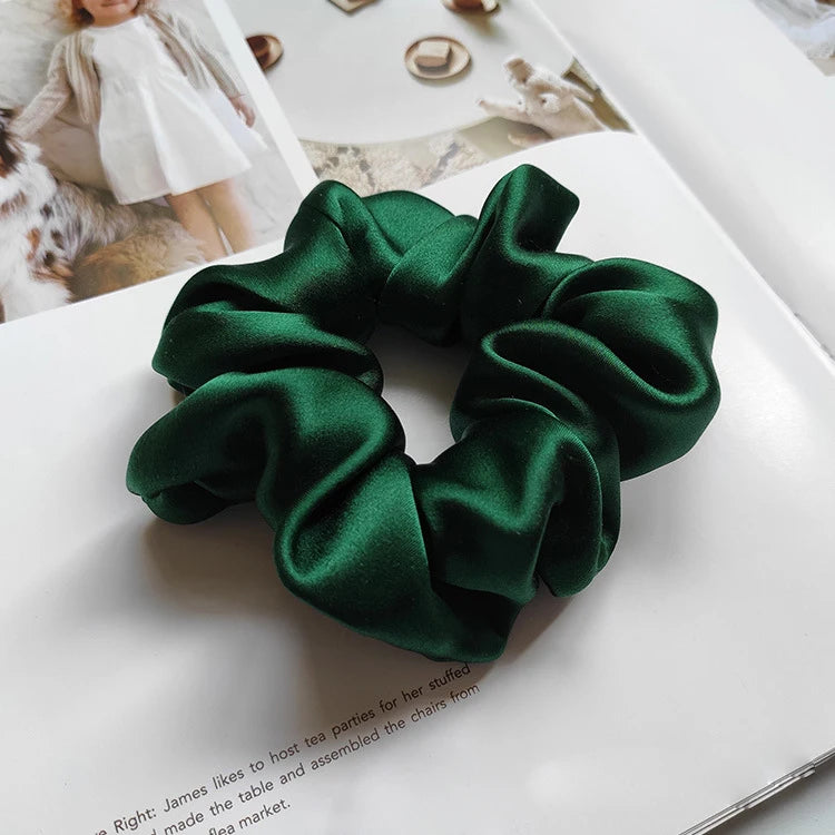 Goma para el pelo de seda verde esmeralda oscura con nudo recogido, mostrada sobre una superficie blanca.