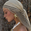 A model wearing a beige bohemian lace trim shawl scarf and gold earrings, looking to the side against a tree trunk.