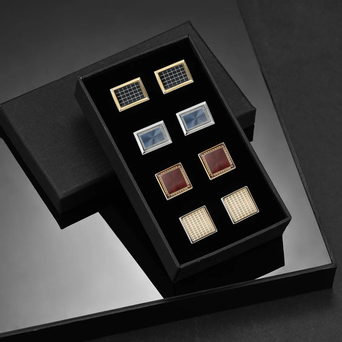 A black presentation box holds various square cufflinks with gold and silver accents.