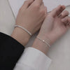 A close-up of a woman's wrist showing two dainty stainless steel heart link bracelets stacked together.