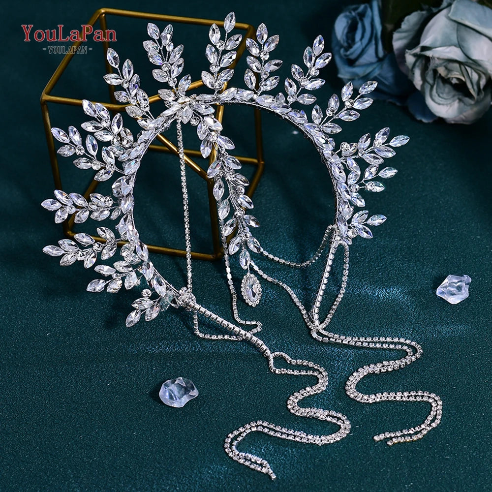 A sparkling rhinestone bridal crown headband with leafy branches and dangling crystals displayed on a dark green fabric.