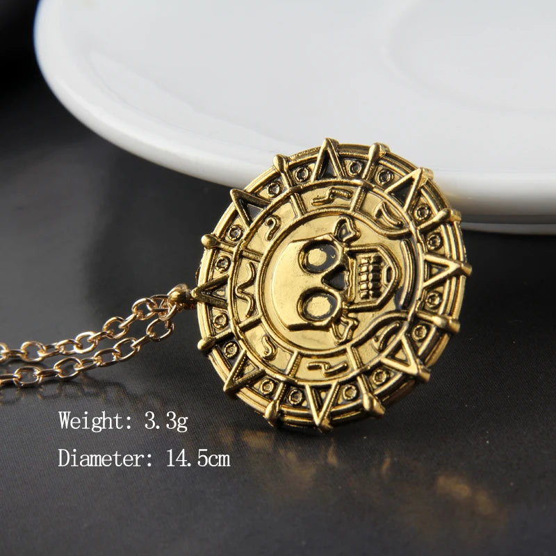 A round gold skull pendant necklace with a chain resting on a dark surface next to a white plate.