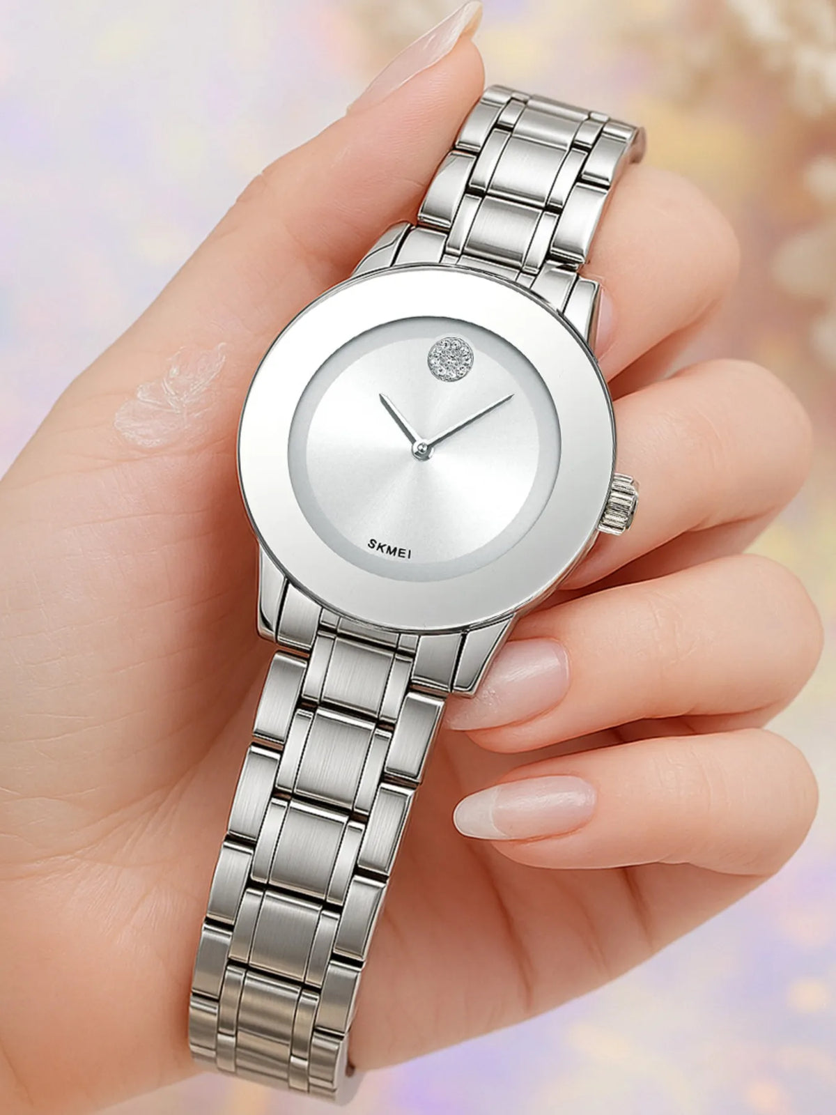 Reloj de cuarzo plateado con pulsera de metal mostrado en la muñeca de una persona.