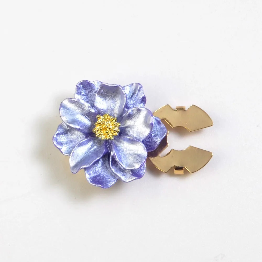 A small, purple iridescent flower button cover with a gold center and a gold clasp.